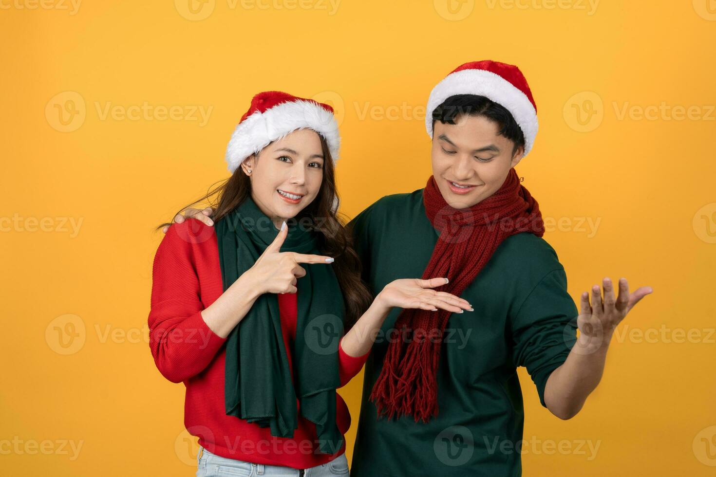 Smiling surprised Asian couple in colorful red and green Christmas clothes on yellow isolated background photo