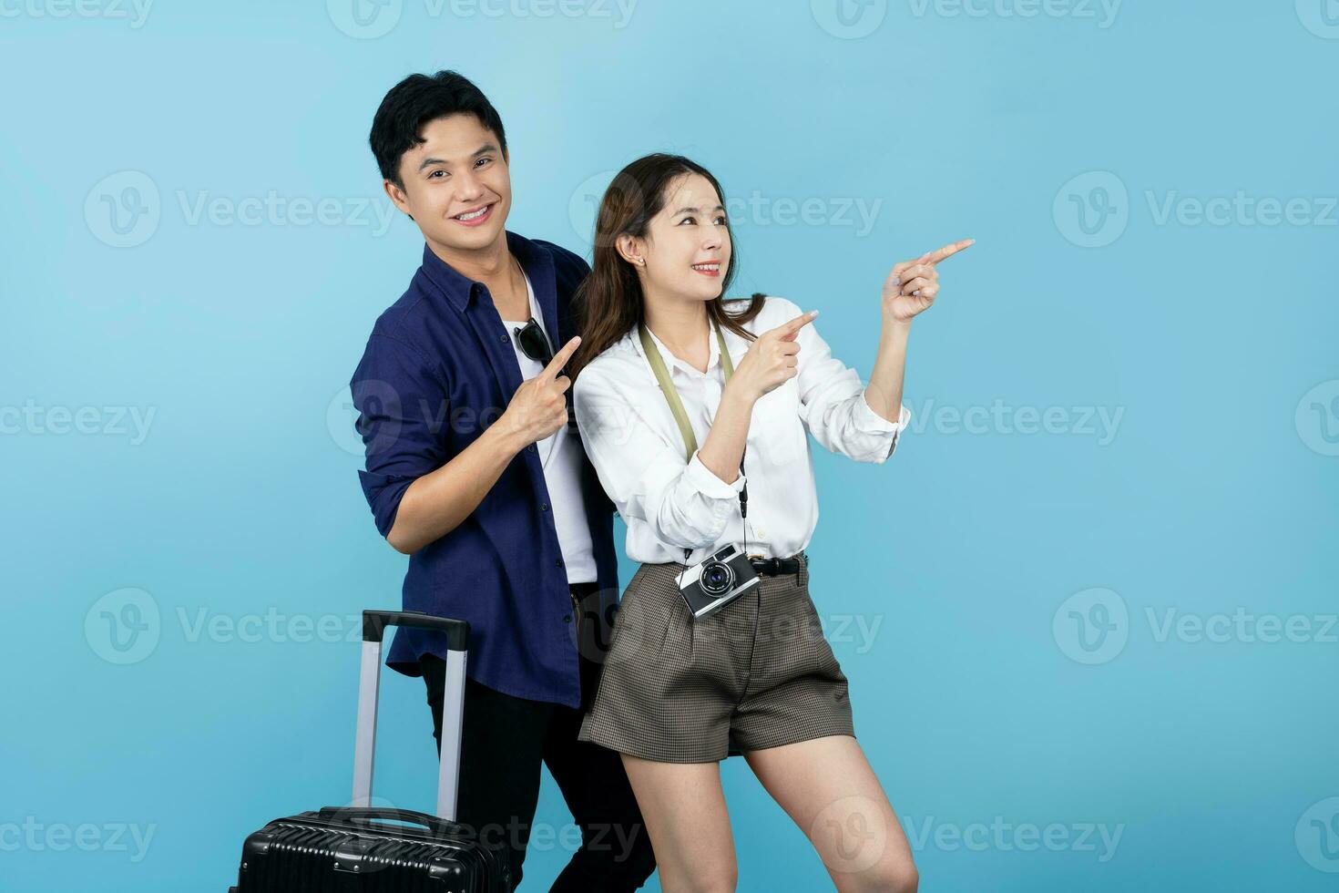 Asian couple with black suitcases and pointing at copy space isolated on blue background photo
