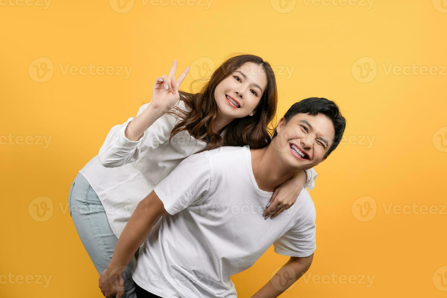 Happy Asian couple in love having fun piggyback ride on yellow background. photo