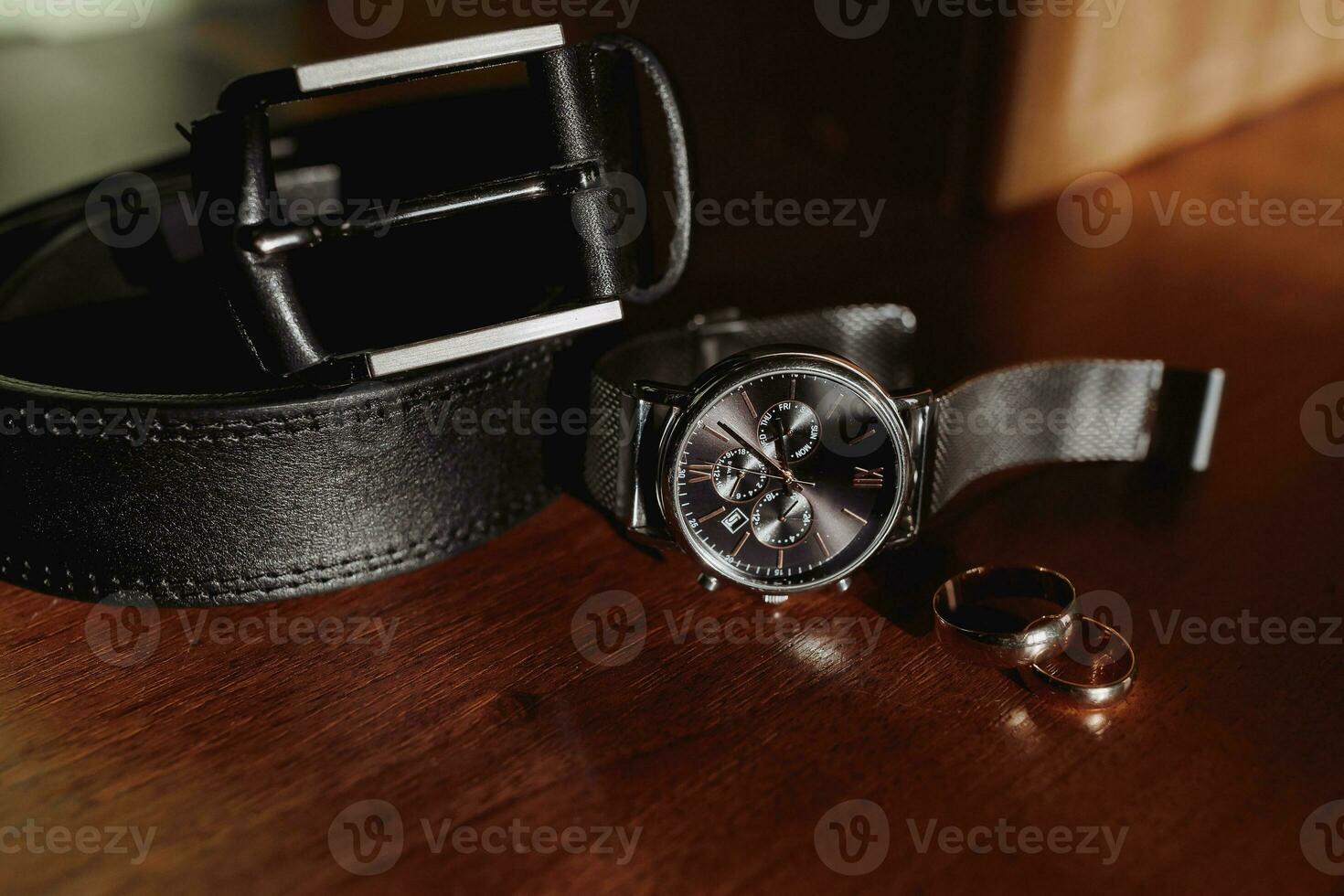 men's details, business, the watch stands stylishly on the table, next to it are wedding rings and a men's leather belt photo