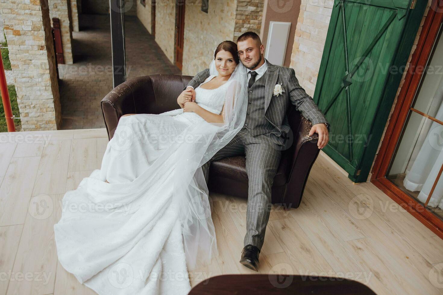 the bride and groom are sitting on a sofa against the background of green windows. Stylish bride and groom. Wedding photo. easy atmosphere photo