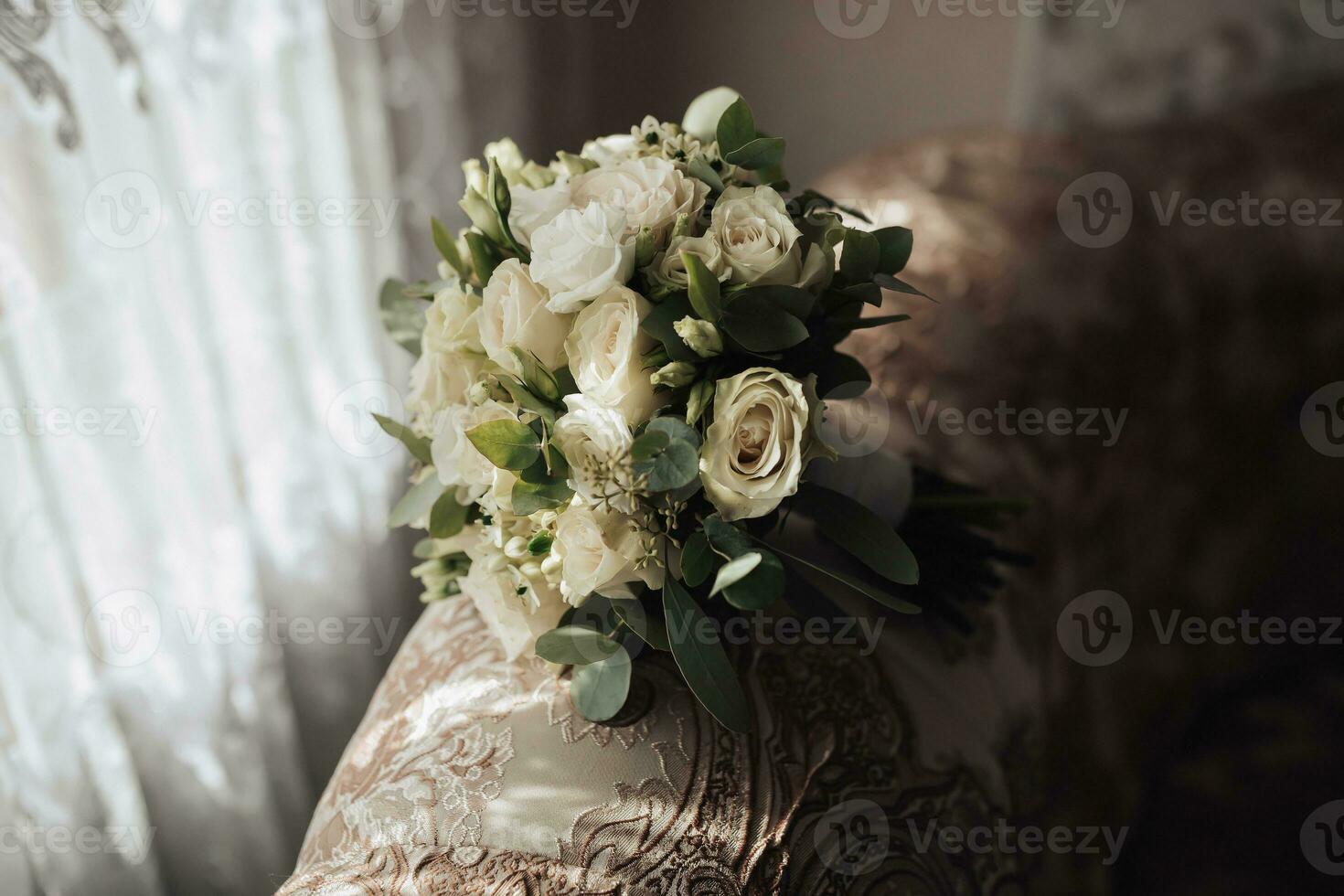 Accessories for the groom's wedding. A bouquet of white roses and greenery stands on the back of the sofa near the window. Beautiful flowers. Light and shadows photo