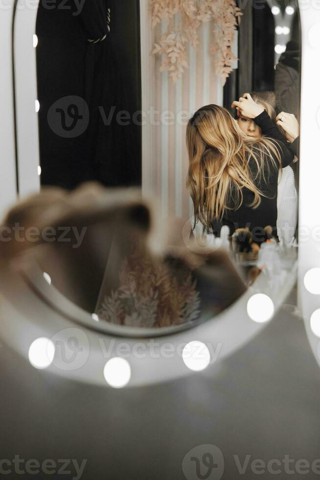 Stylish bride is doing makeup in the morning. A makeup artist makes eyebrows and applies shadows to the face of the bride, which is reflected in the mirror. Morning of the bride. Hairdo. photo