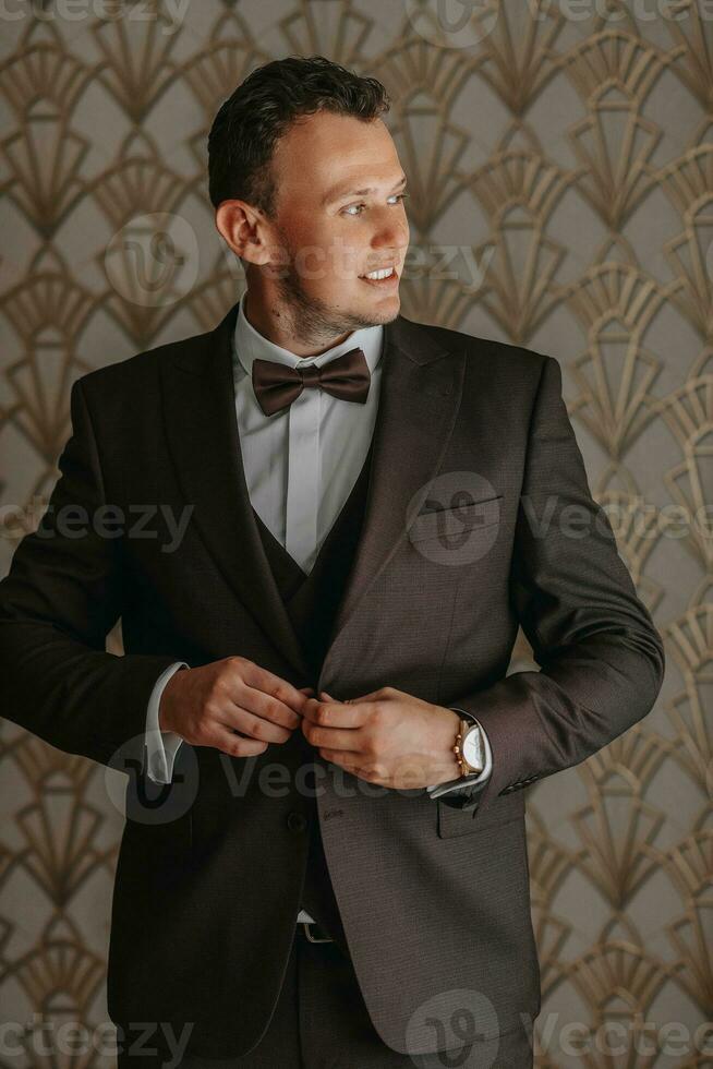 Confident elegant business man buttoning up a brown jacket while looking out the window. portrait in the room. photo