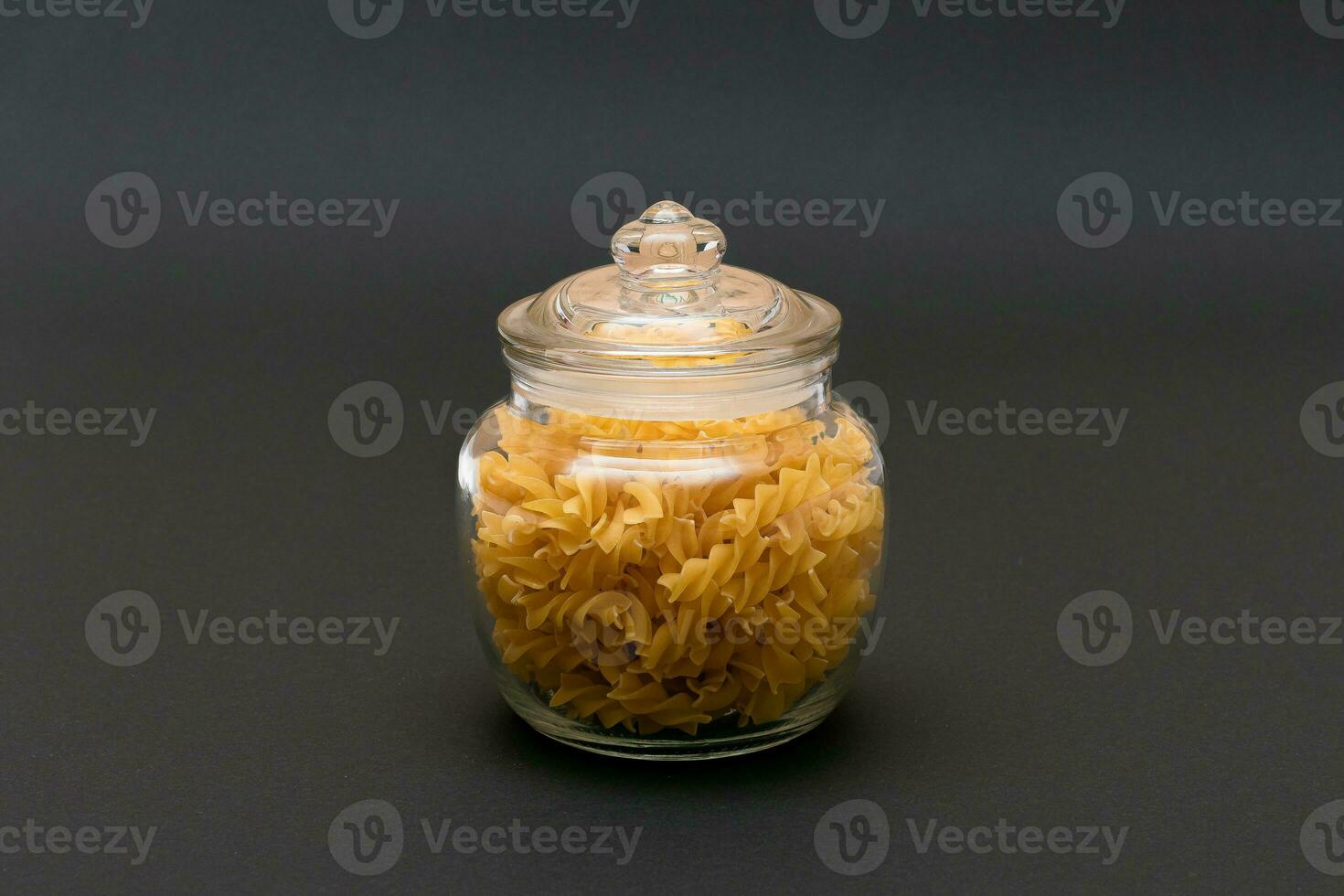 Uncooked Fusilli Pasta in Glass Jar on Black Background. Raw and Dry Macaroni. Unhealthy and Fat Food. Italian Culture photo