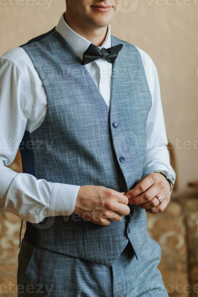 Morning of the groom and details, white shirt, blue vest, good light, young man, stylish groom getting dressed, getting ready for the wedding ceremony. close-up of male hands photo