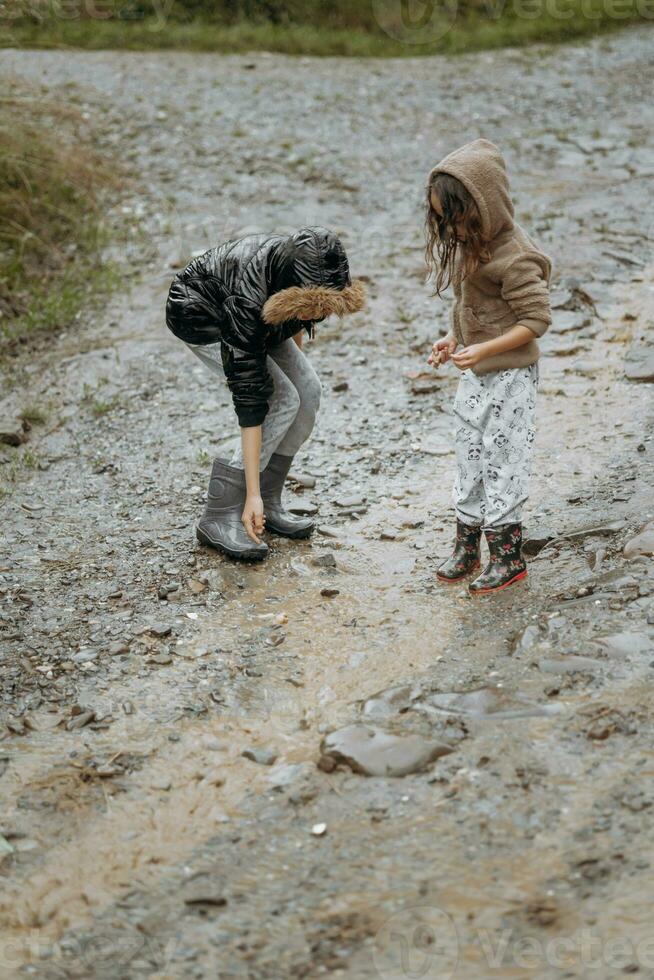 two happy little girls of European appearance playing in puddles during rain in summer. children are playing in the rain. child playing in nature outdoors. the girl enjoys the rain. photo