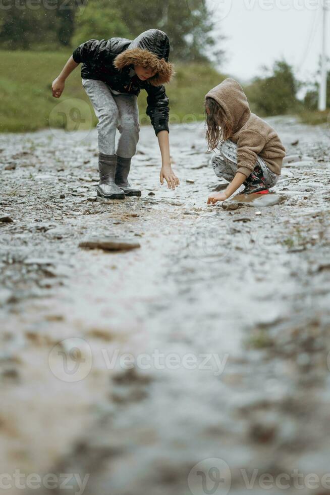 two happy little girls of European appearance playing in puddles during rain in summer. children are playing in the rain. child playing in nature outdoors. the girl enjoys the rain. photo