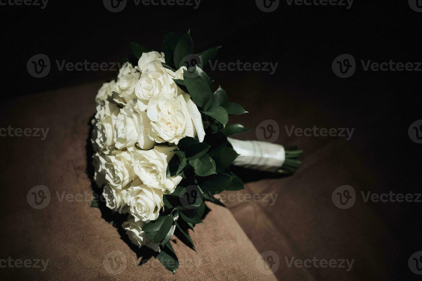 A bouquet of white roses and greenery on a brown background. A beautiful photo with details of the wedding. Wedding day. Contour light. Shadows and light