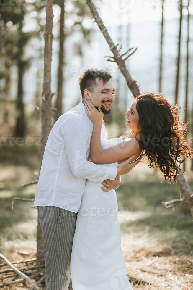Stylish groom in white shirt and cute brunette bride in white dress in forest near wedding wooden arch. Wedding portrait of newlyweds. photo