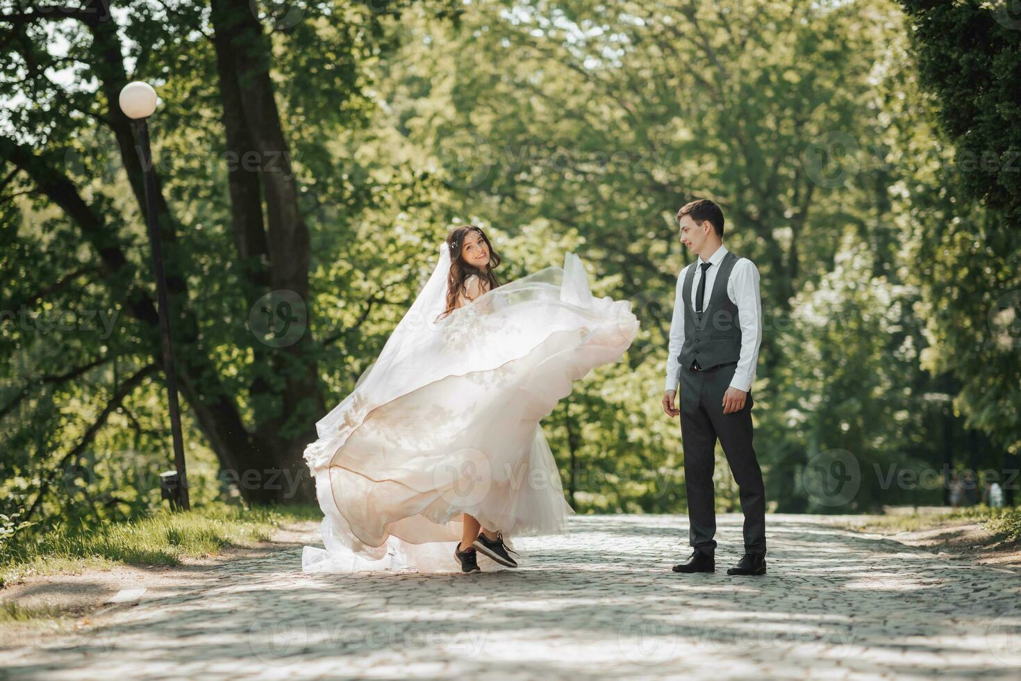 Groom and bride in the garden. Spring wedding in the park. Happy wedding couple running in the park. The bride is circling with her dress. Stylish and beautiful. Photo from the back. Princess dress.