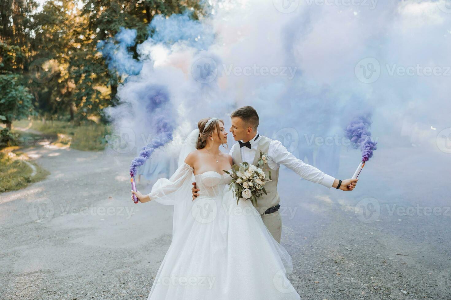 In their hands, the newlyweds hold multi-colored smoke bombs of blue color. Groom and bride kiss. Wedding fun. photo