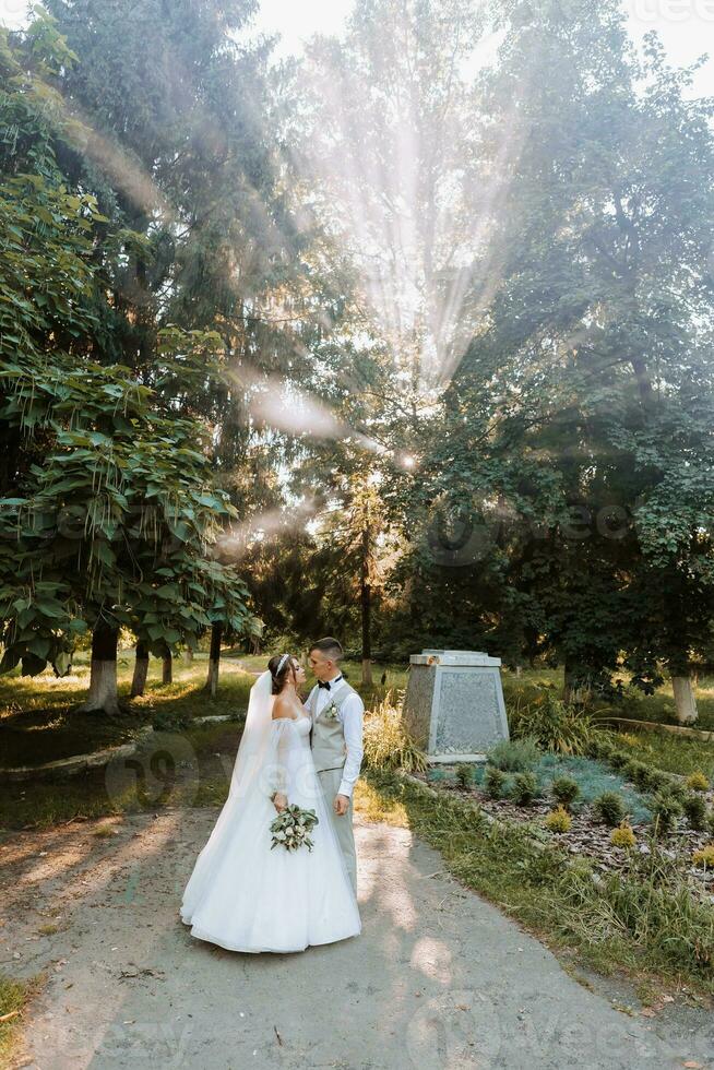 beautiful couple in love on their wedding day. A walk in the park in the sunlight through the leaves of the trees, the bride and groom embrace. Amazing kisses and hugs photo