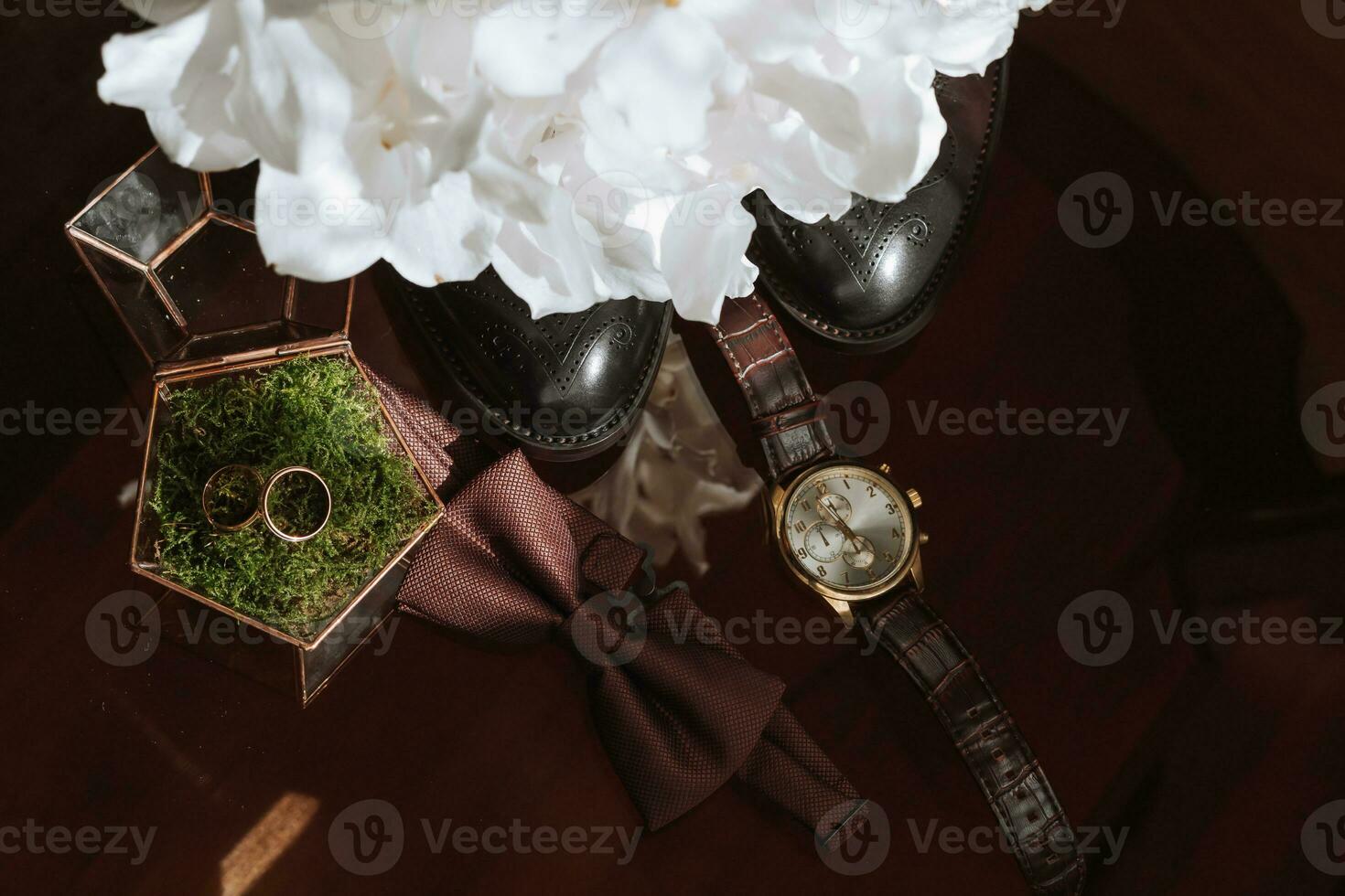 Morning of the groom and details, details of the groom on a dark background. men's watch, wedding rings in a glass box and wooden moss, a men's butterfly and a bouquet of white flowers photo