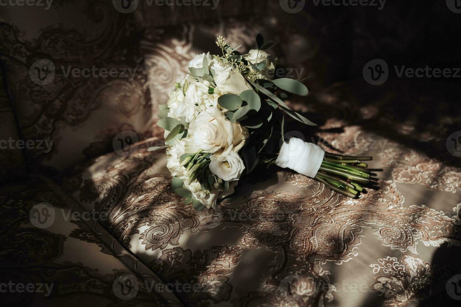 Accessories for the groom's wedding. A bouquet of white roses and greenery stands on the back of the sofa near the window. Beautiful flowers. Light and shadows photo
