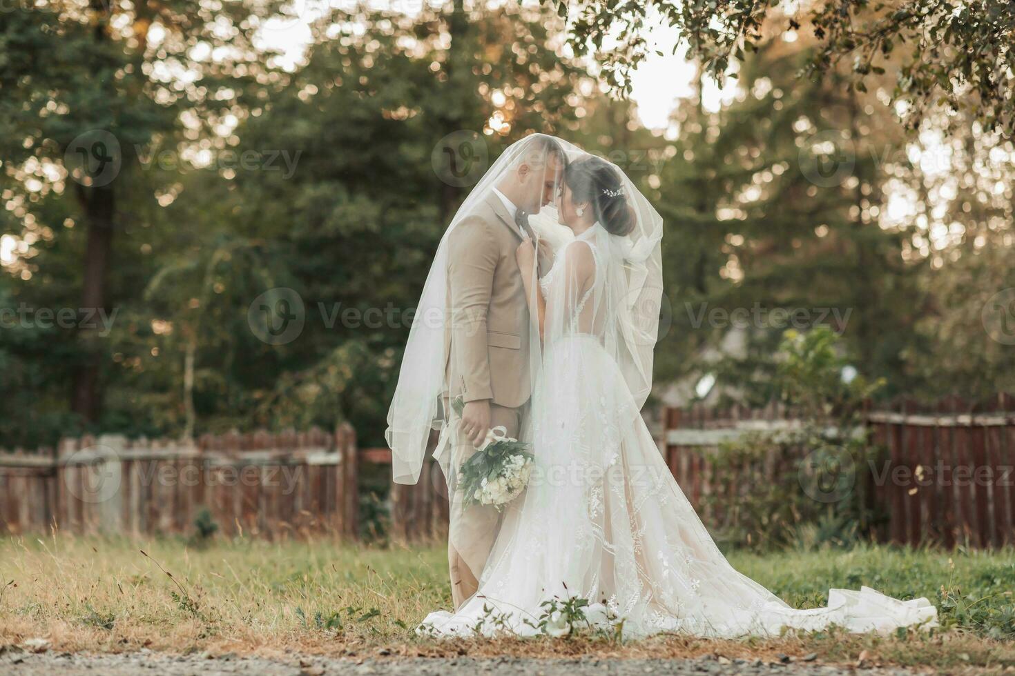 Wedding portrait of the bride and groom. Happy bride and groom gently hug each other under the veil, pose and kiss. Stylish groom. Beautiful young bride photo