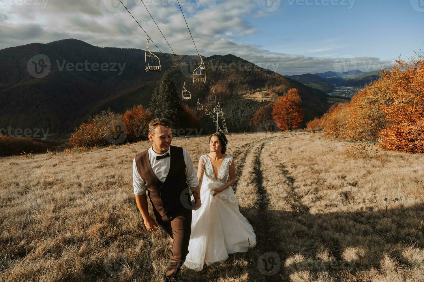 Wedding couple walks in the mountains. The groom leads the bride by the hand. The dress of the bride develops in the wind. photo