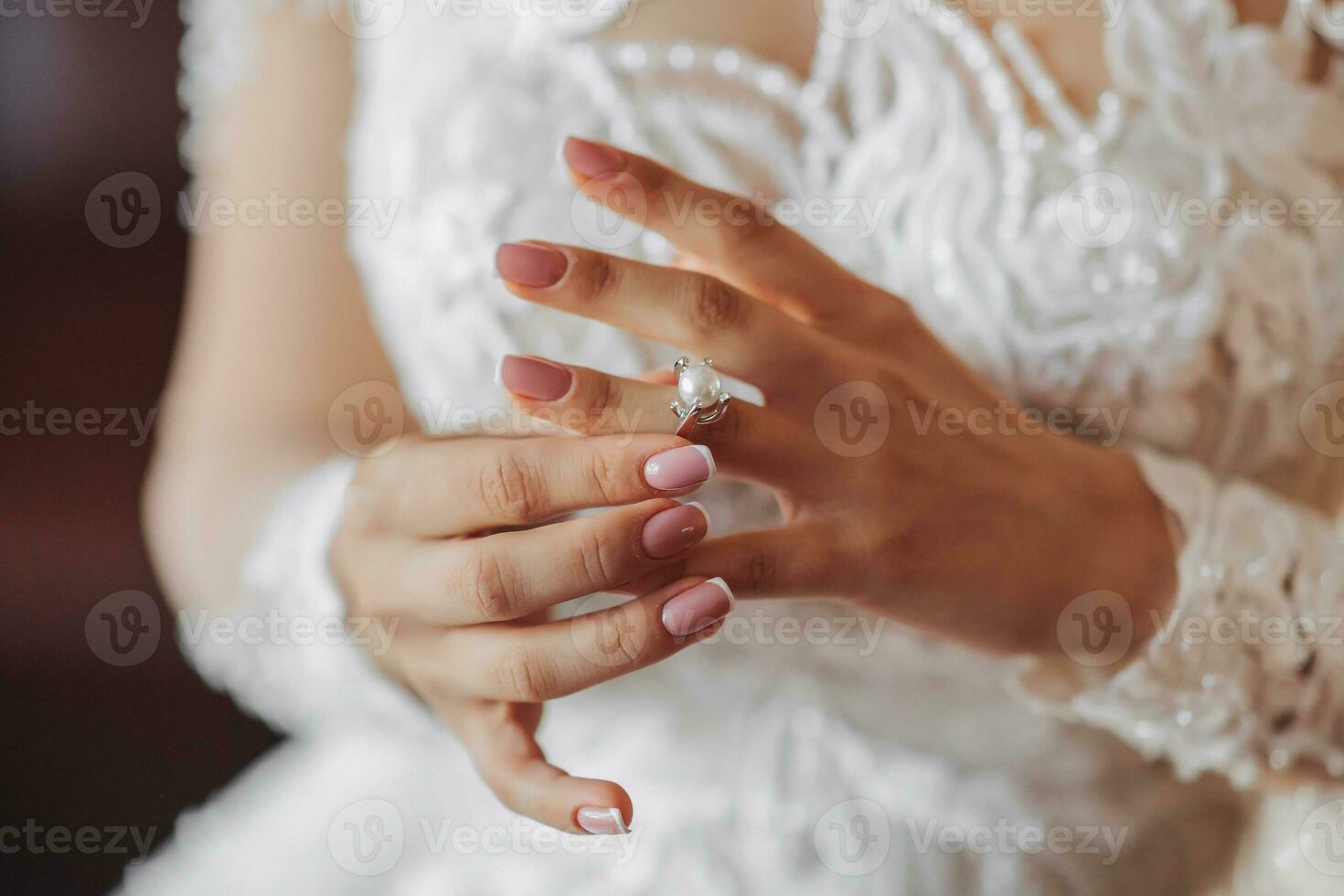 rubia novia en largo manga cordón vestir en pie en su habitación, posando y poniendo en su compromiso anillo. hermosa pelo y constituir, abierto espalda. Boda retrato. francés manicura foto