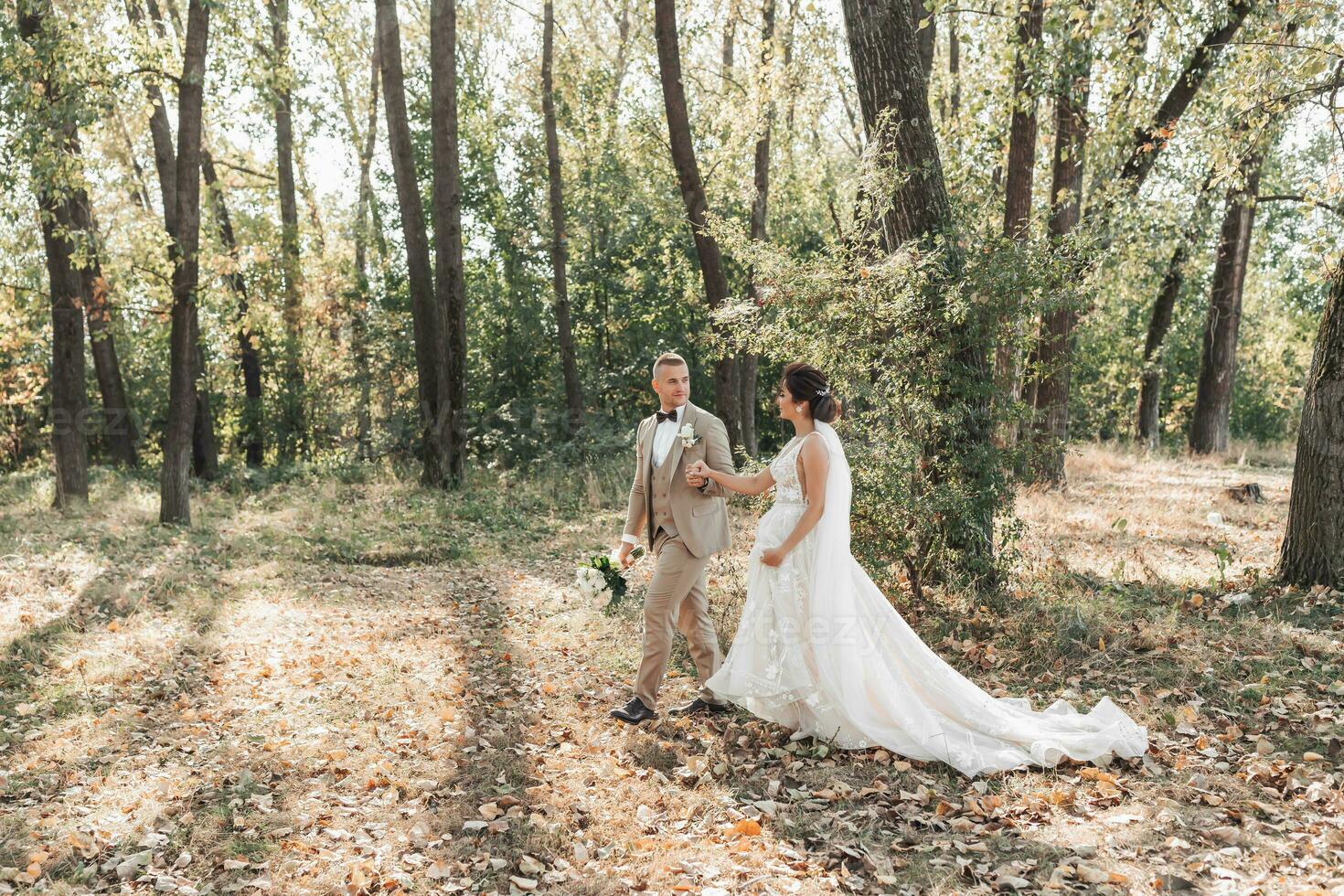 Wedding photo. The bride and groom are walking in the forest, holding hands and looking at each other. The groom is holding a bouquet. Couple in love. Summer light. The shadows photo