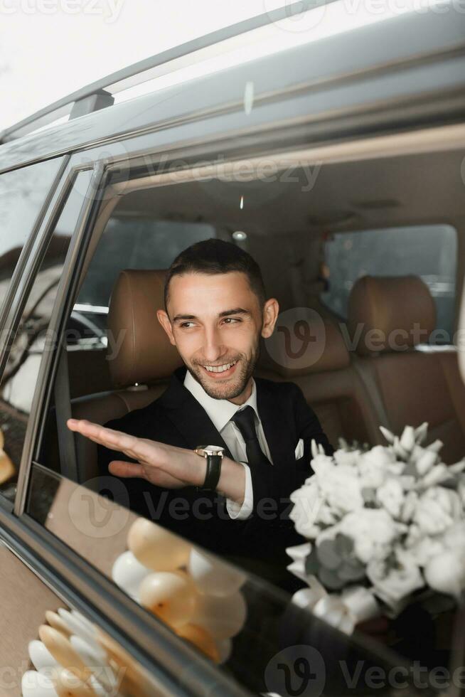 A stylish groom, preparing for the wedding ceremony, sits in a car. Groom's morning. Businessman wearing a jacket, male hands close-up, groom getting ready in the morning before the wedding ceremony photo