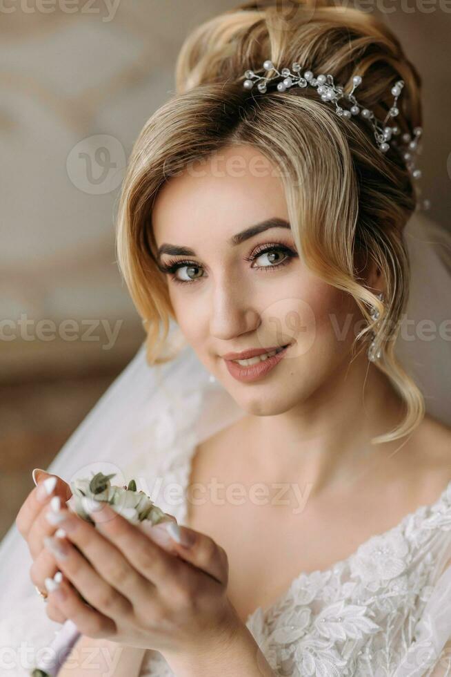 Wedding details. The bride in a white dress holds the groom's wedding boutonniere and looks into the lens. Beautiful hands. French manicure. Beautiful hair and makeup. Diadem photo