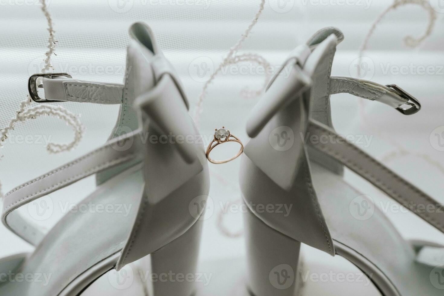The bride's wedding ring stands between elegant white shoes on a light background. Bride's shoes and wedding ring. Wedding photography photo