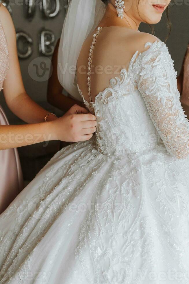 Mañana novia. dama de honor Ayudar el novia cordones arriba su vestido. novias ayuda el novia a sujetar un vestir foto