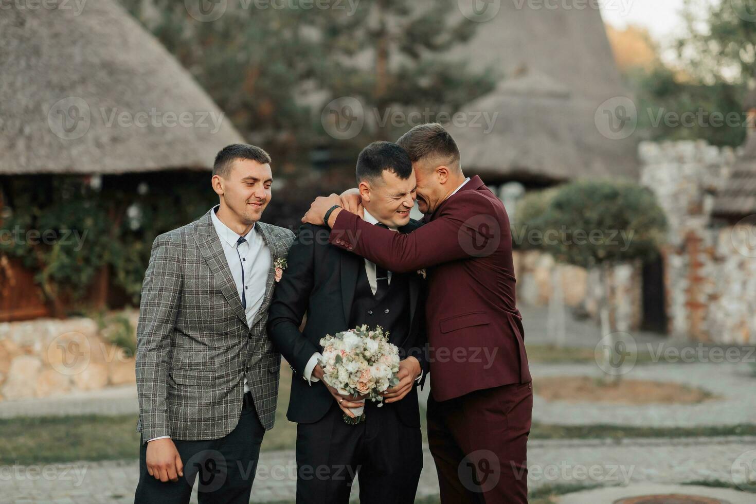 Photo of three men in classic suits. A man holds a bouquet while standing among his friends. Business style. Stylish men