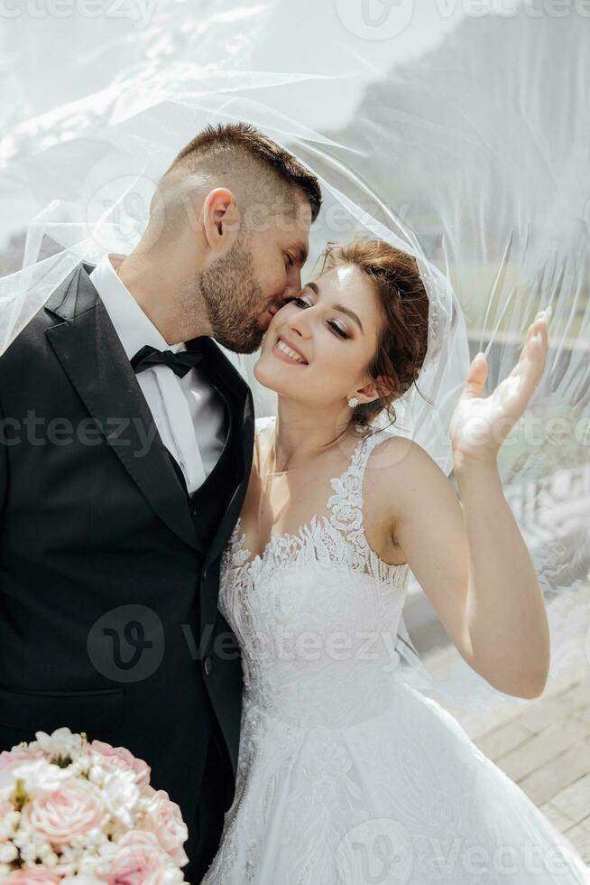 elegant beautiful couple under veil. Hugs on each other. The bride hugs and kisses the groom. Gorgeous light adds a romantic atmosphere photo