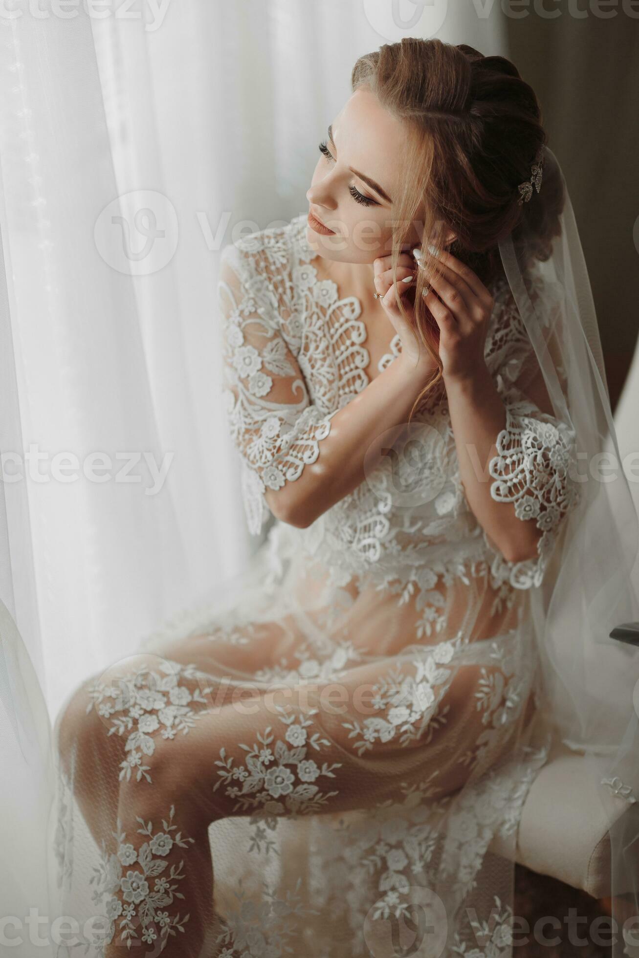 the bride in a transparent robe sits on the edge of a soft pink chair in a  bright room, wears an elegant gold earring 36423751 Stock Photo at Vecteezy