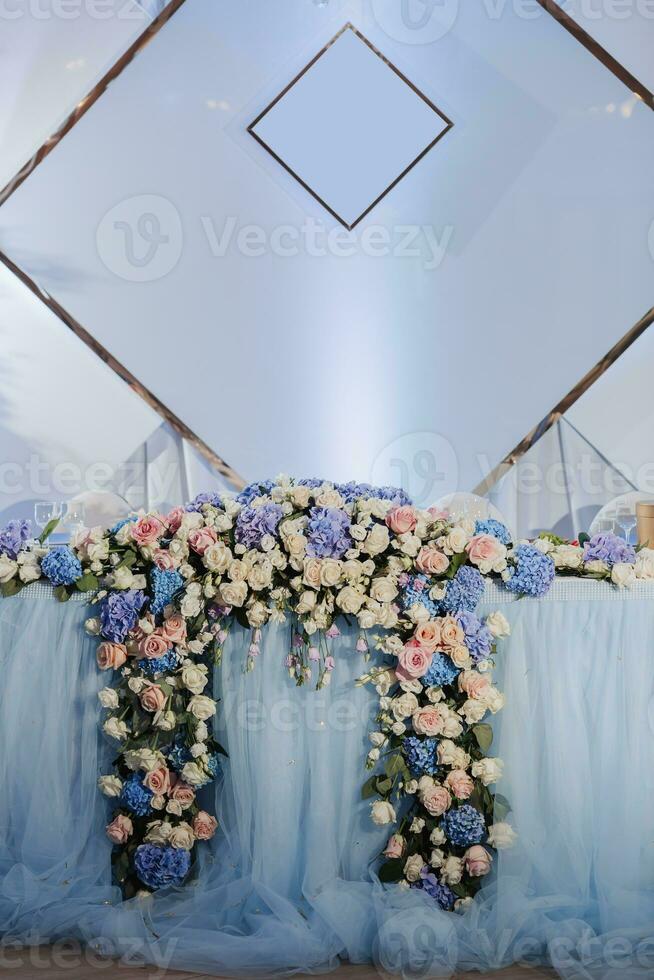 The wedding table of the bride and groom, decorated with flowers, is made in blue and silver. Candles on stands. White flowers and greenery. Silver. Wedding details photo