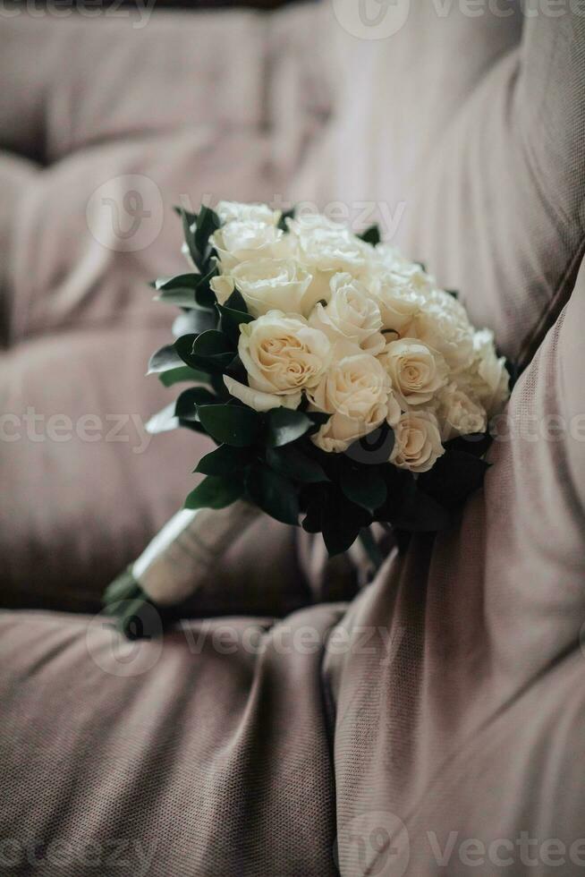 A bouquet of white roses and greenery on a brown background. A beautiful photo with details of the wedding. Wedding day. Shadows and light