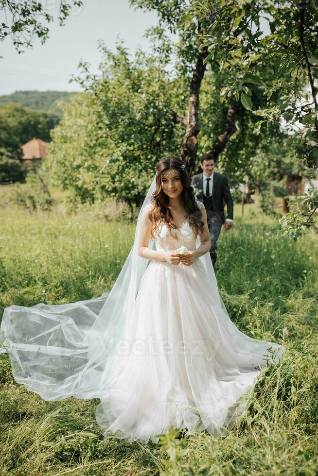 The first wedding meetings in the garden. A meeting of newlyweds on a green field in the open air, a surprise in nature. Front view of smiling bride waiting for groom. Wedding ceremony in the forest. photo