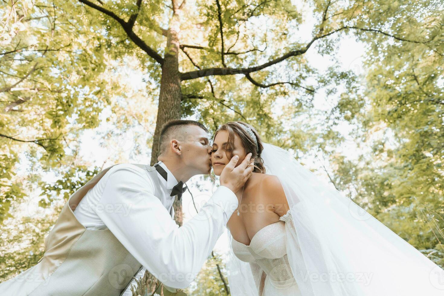 retrato de un hermosa Pareja en amor en tu Boda día. un caminar en el parque en el luz de sol. increíble Besos y abrazos de el novia y novio con un ramo de flores foto