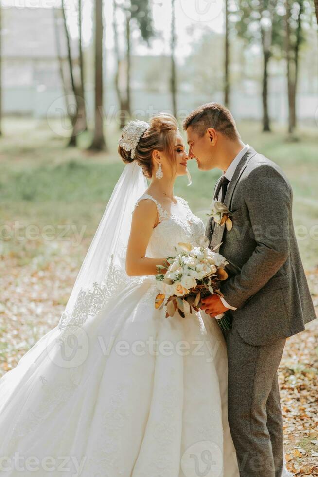 Fashionable groom and cute blonde bride in a white dress with a crown, a bouquet are hugging, laughing in the park, garden, forest outdoors. Wedding photography, portrait of smiling newlyweds. photo