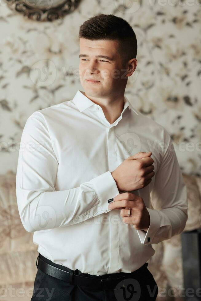 Handsome Man buttons up the sleeve of a white shirt and poses for the camera. Front view. Daylight. Fashion and style. Business. Men's style. Beautiful hands photo