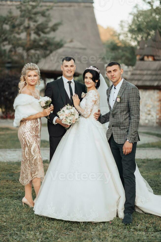 frente ver de recién casados caminando mano en mano entre amigos. muchachas en dorado vestidos sostener ramos de flores, el novia en un voluminoso vestido, el novio y su amigos en trajes. Boda en naturaleza foto