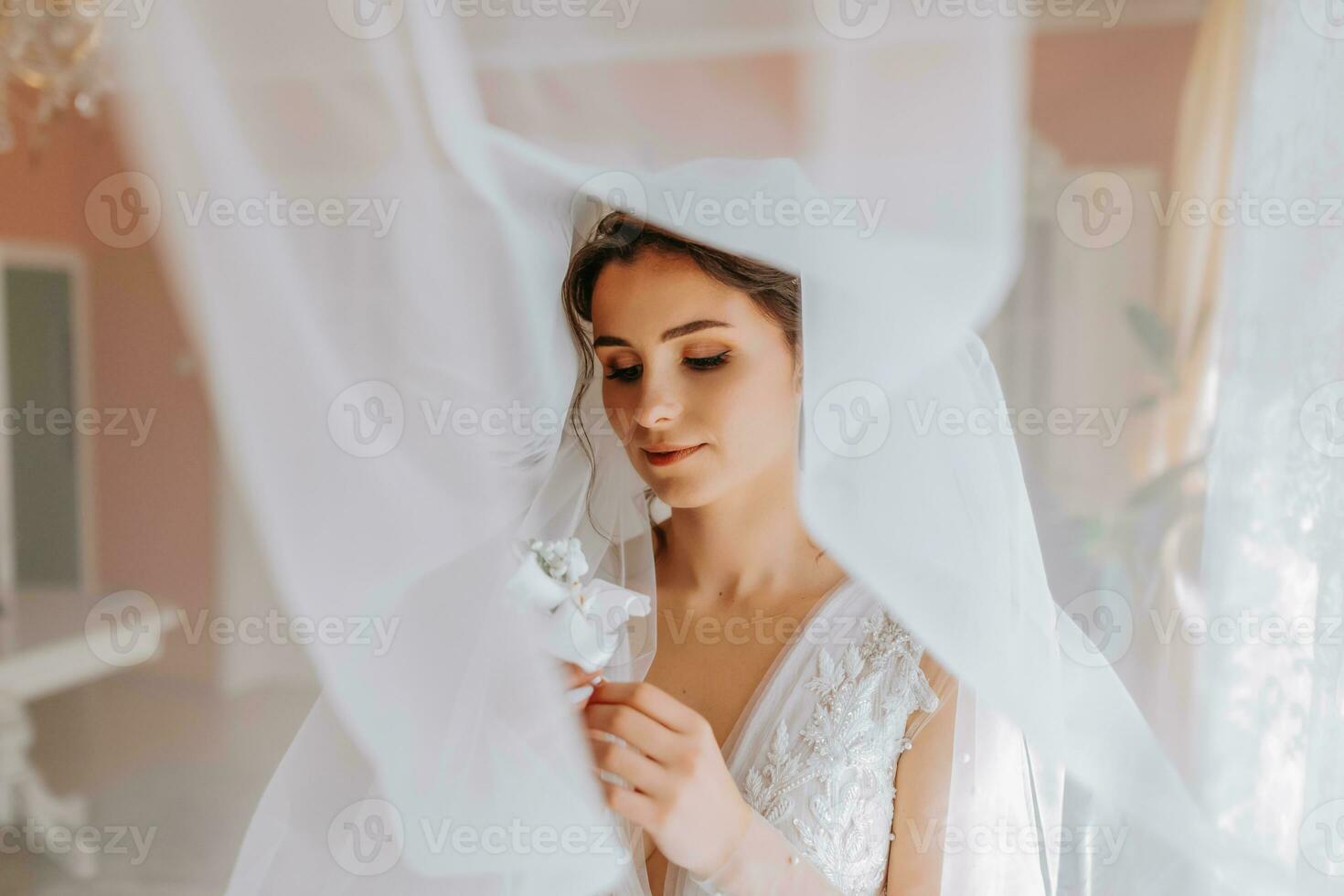 A brunette bride in a white dress holds her wedding bouquet, poses. French manicure. Open shoulders. Beautiful hands. Long veil. Morning of the bride. Details photo