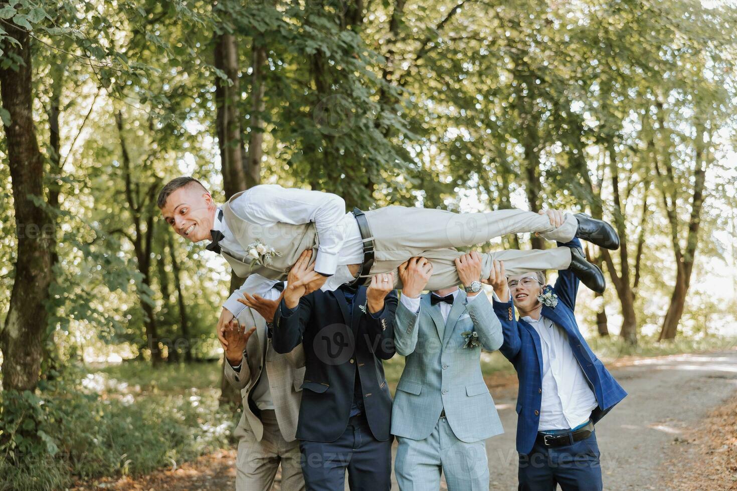 A group of friends lifts the happy groom to the top, the company of the groom's friends celebrate together in the park photo