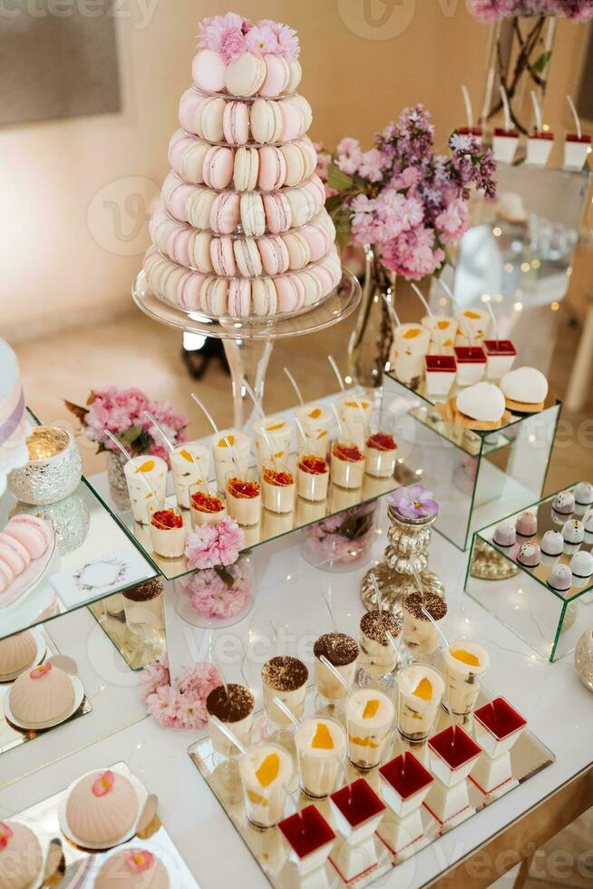 delicioso Boda recepción caramelo bar postre mesa lleno con pasteles y dulces y flores chino Cereza flores en el antecedentes de un Exquisito restaurante foto