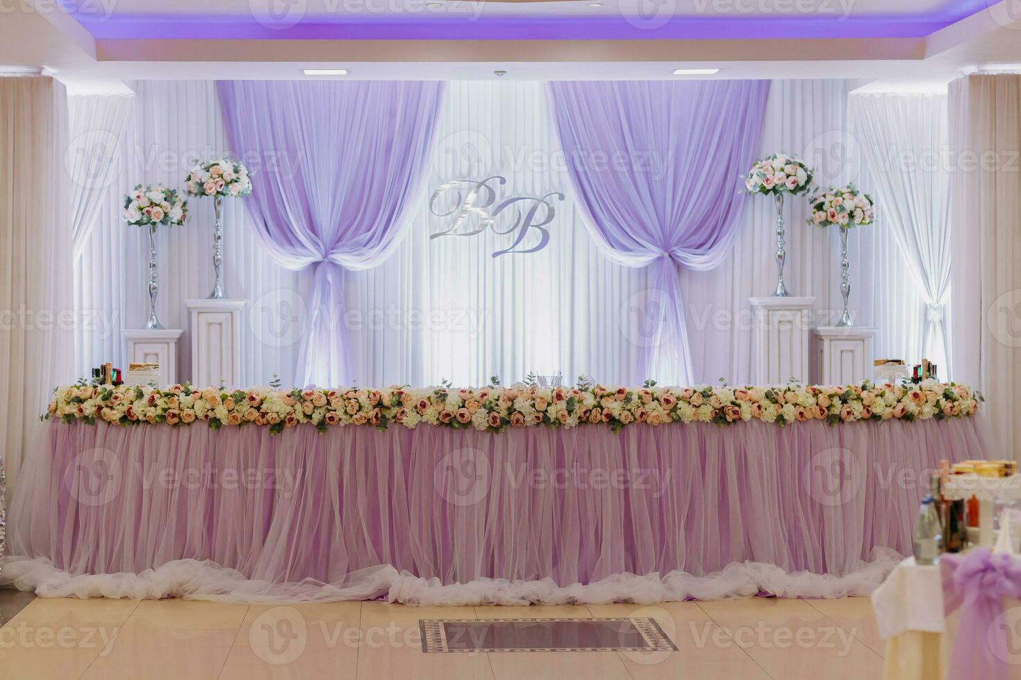 The wedding table of the bride and groom, decorated with flowers, is made in purple. Flowers on stands. Wedding details photo