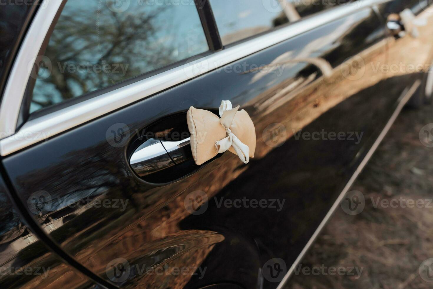 Cropped photo of a black car. A soft pink bow is attached to the handle of the black machine. Details. Business style. Expensive cars