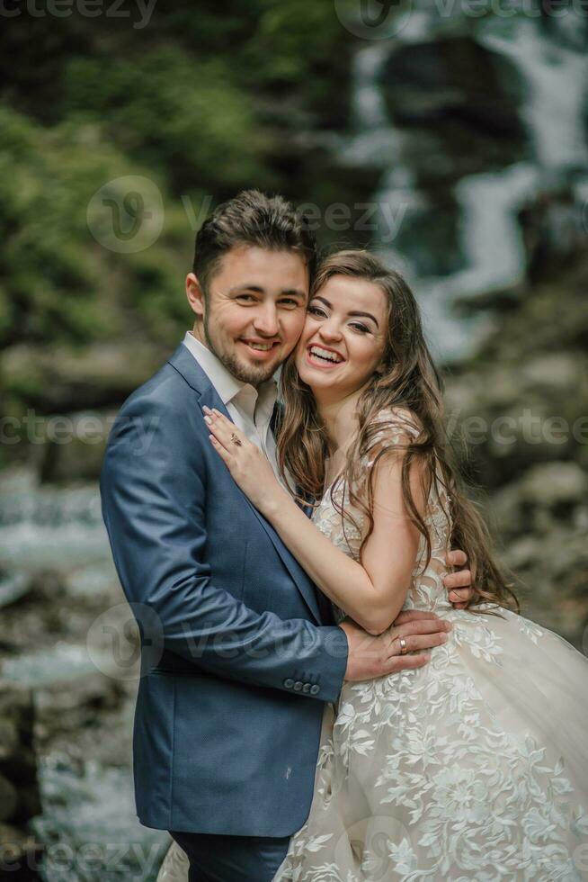 Portrait of a happy bride and groom near a waterfall. Bride and groom. Wedding photo session in nature. Photo session in the forest of the bride and groom.