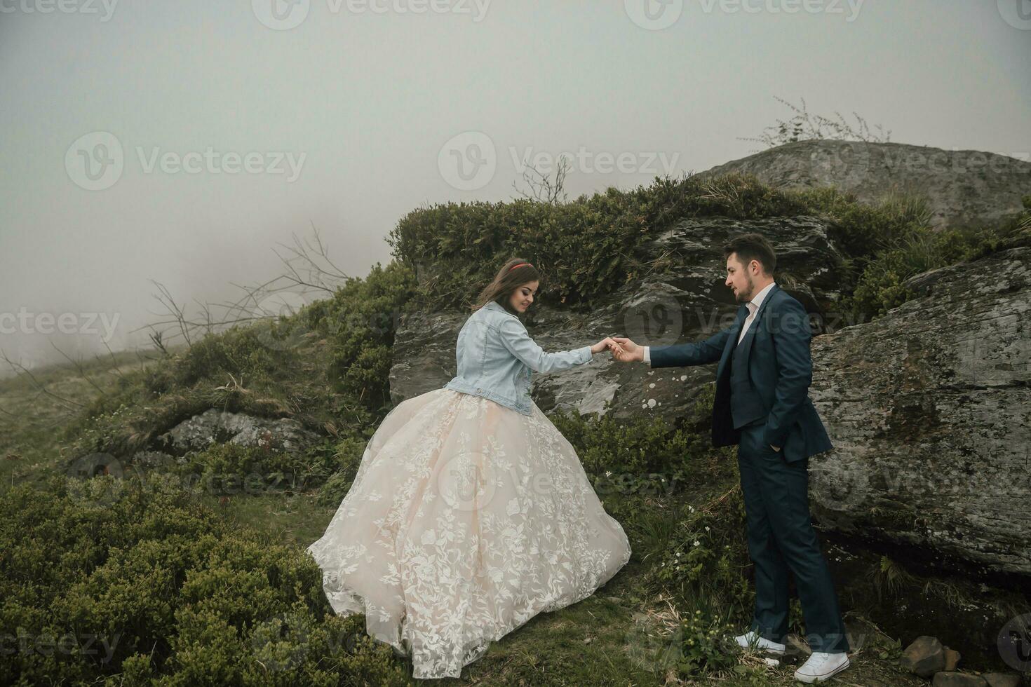 contento Boda Pareja en el montañas cerca un grande Roca participación manos. Boda foto sesión en naturaleza. foto sesión en el bosque de el novia y novio.