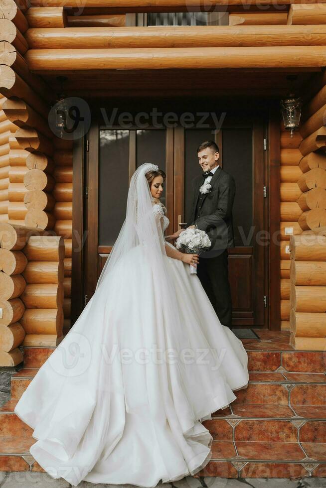 Handsome groom and charming bride stay together near modern wooden house in park photo