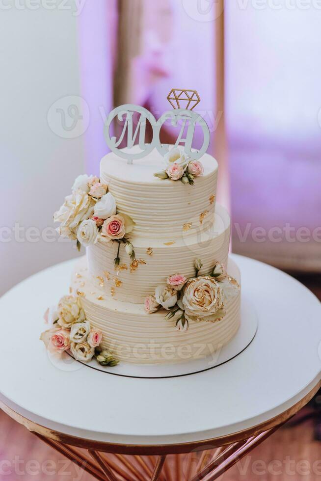 White wedding cake with flowers and blueberries. A beautiful home wedding three-tiered cake decorated with pink roses in a rustic style on wooden table photo