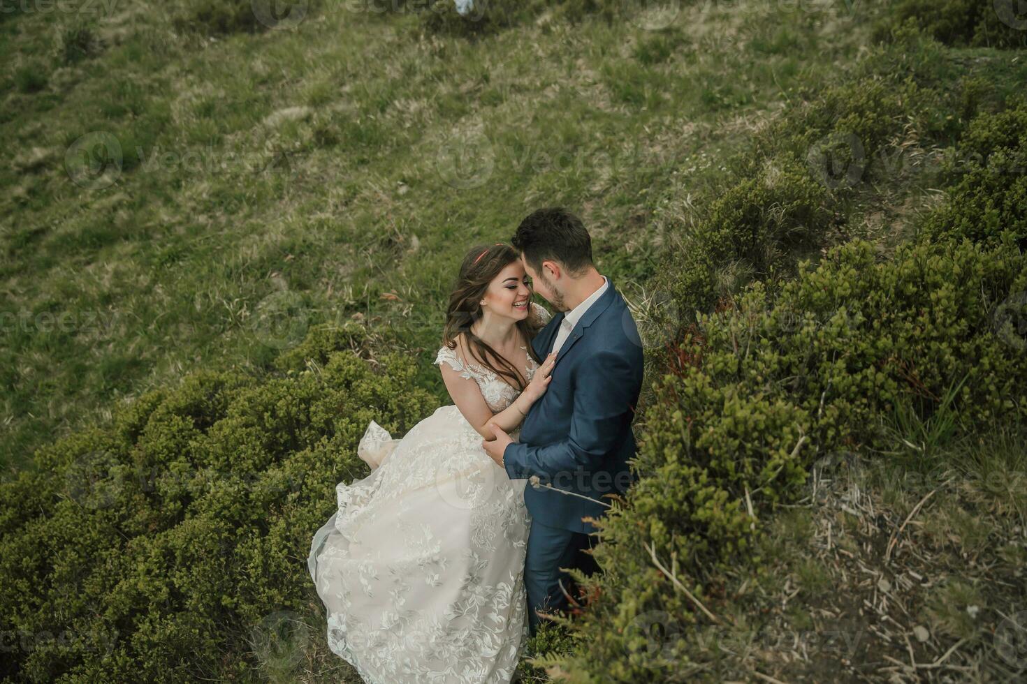 Happy wedding couple in the mountains. The bride with her long hair blowing in the wind smiles sincerely. Wedding photo session in nature. Photo session in the forest of the bride and groom.