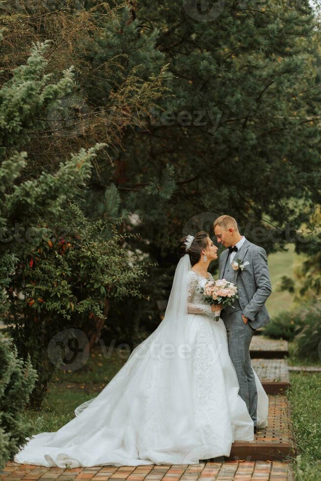 Handsome groom and charming bride together in the park. Portrait. Luxurious dress with a long train. Elegant young groom. Wedding bouquet. luxury wedding photo