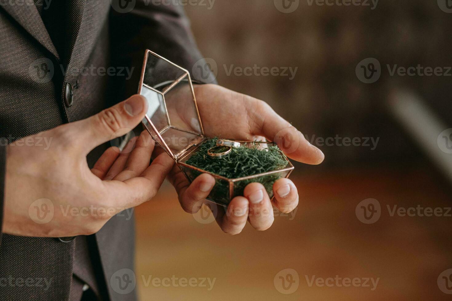 Wedding gold rings on a decorative glass box with wooden green moss, standing in the hands of the groom, close-up. Jewelry concept photo