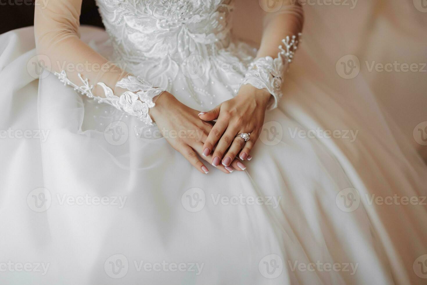 Cropped photo. Beautiful hands with a lace sleeve on a white wedding dress. Wedding portrait. French manicure photo